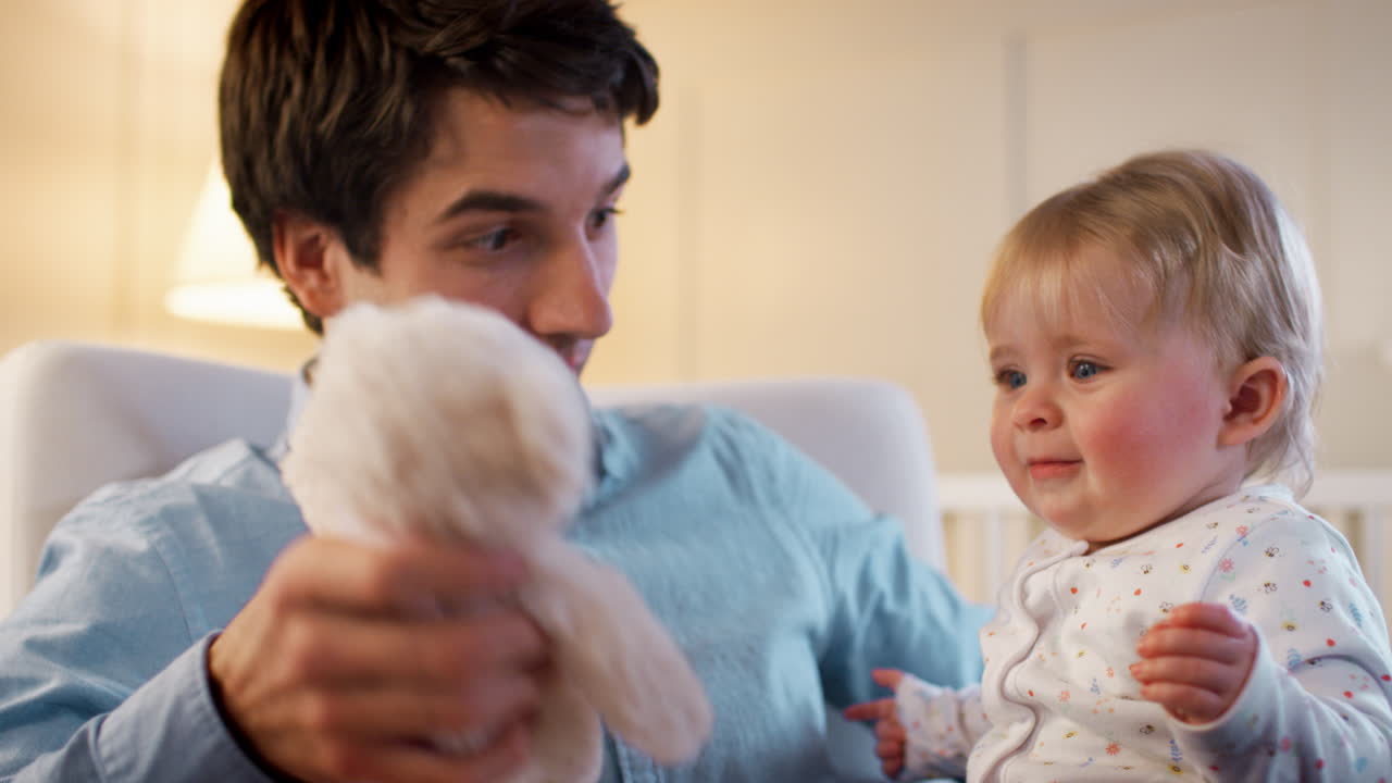 Evde, yatma zamanında bebek odasında peluş oyuncakla oynayan baba ve kız bebek