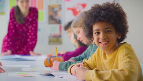 retrato de un estudiante masculino escribiendo en un libro de ejercicios en un aula multicultural