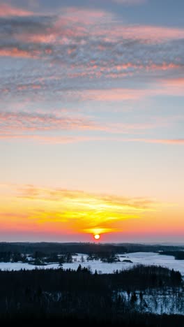stunning winter sunrise over snow covered forest in countryside landscape. vertical drone hyperlapse of sunrise over the horizon.