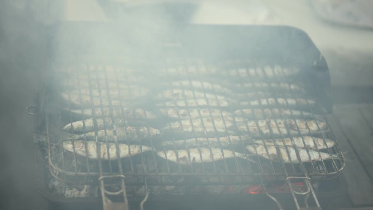 Sardine che grigliano su una griglia a carbone, con fumo che sale, preparando un pasto sano all'aperto