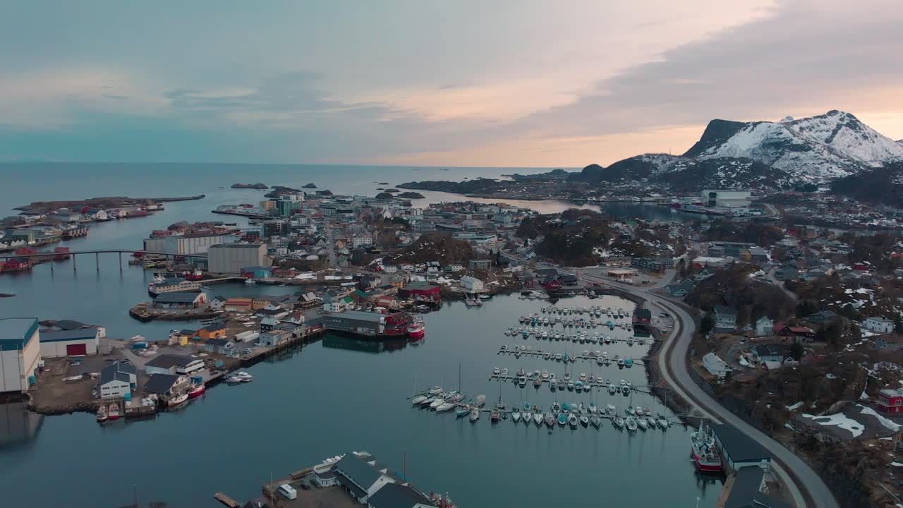 Aerial drone shot of a orange sunset behind a mountain chain in Lofoten, Norway. With a small fishing village with boats