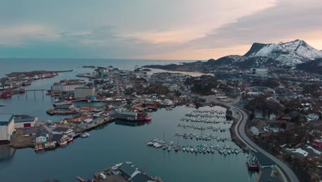 aerial drone shot of a orange sunset behind a mountain chain in lofoten, norway. with a small fishing village with boats