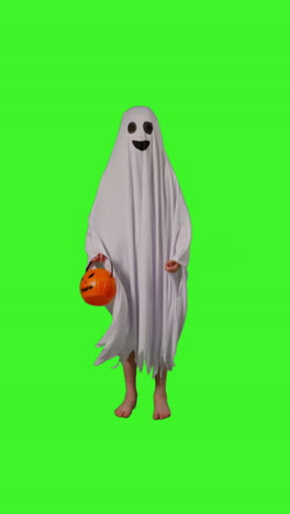 Vertical-Video-Full-Length-Shot-Of-Child-Dressed-Up-In-Ghost-Costume-Knocking-On-Door-Trick-Or-Treating-At-Halloween-Holding-Pumpkin-Shaped-Jack-O'Lantern-Bucket-Against-Studio-Green-Screen