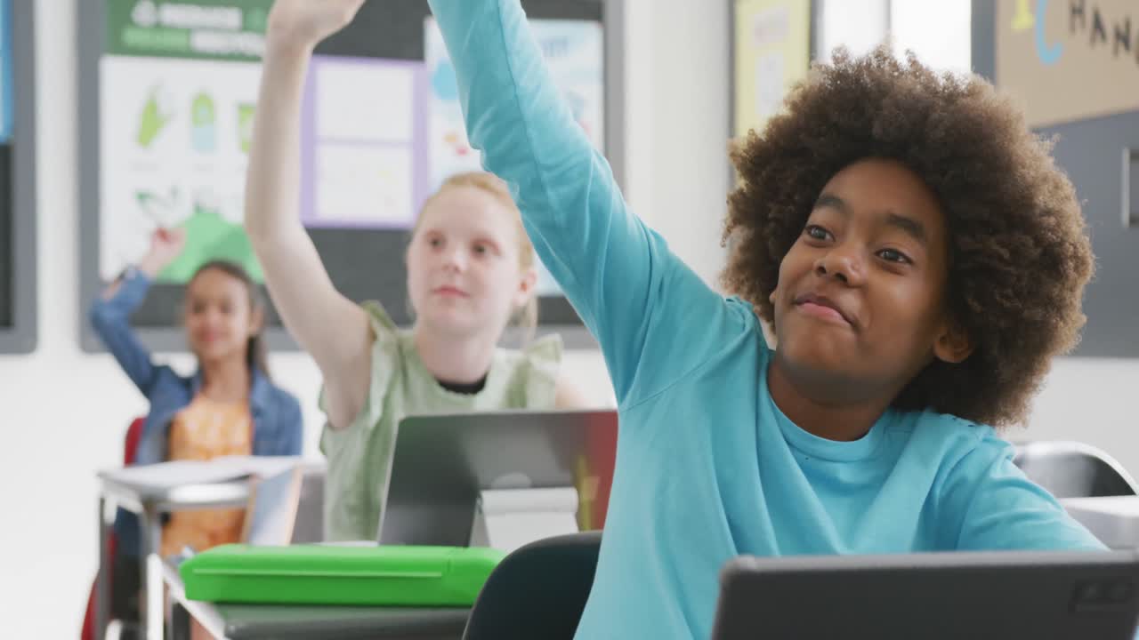 video de un escolar afroamericano sonriente en el escritorio levantando la mano en una clase diversa, espacio de copia.