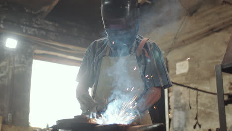 blacksmith in helmet welding iron in smithy