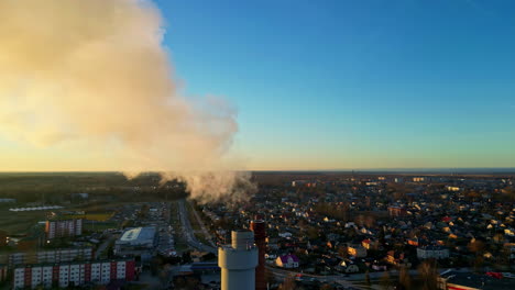 vista aérea de los humos que salen de una chimenea industrial cerca de una zona residencial