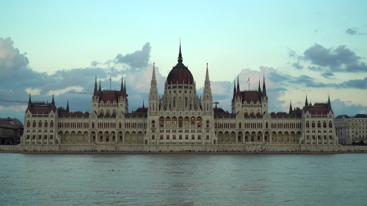People walk on the closed lower quay due to the high water level of the River Danube in front of the Hungarian Parliament Building during dusk in Budapest, Hungary.