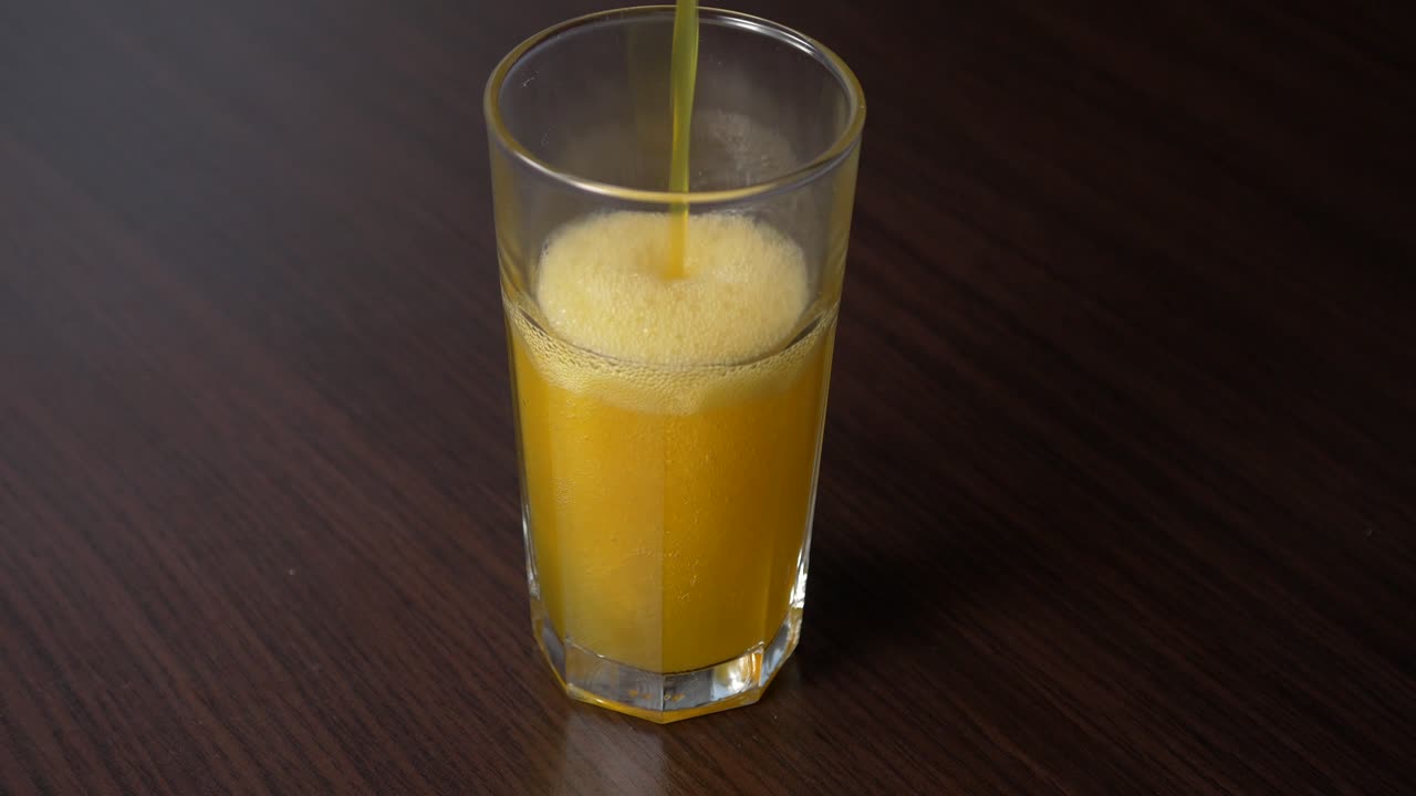 Versamento di aranciata frizzante in un bicchiere alto su un tavolo di legno.