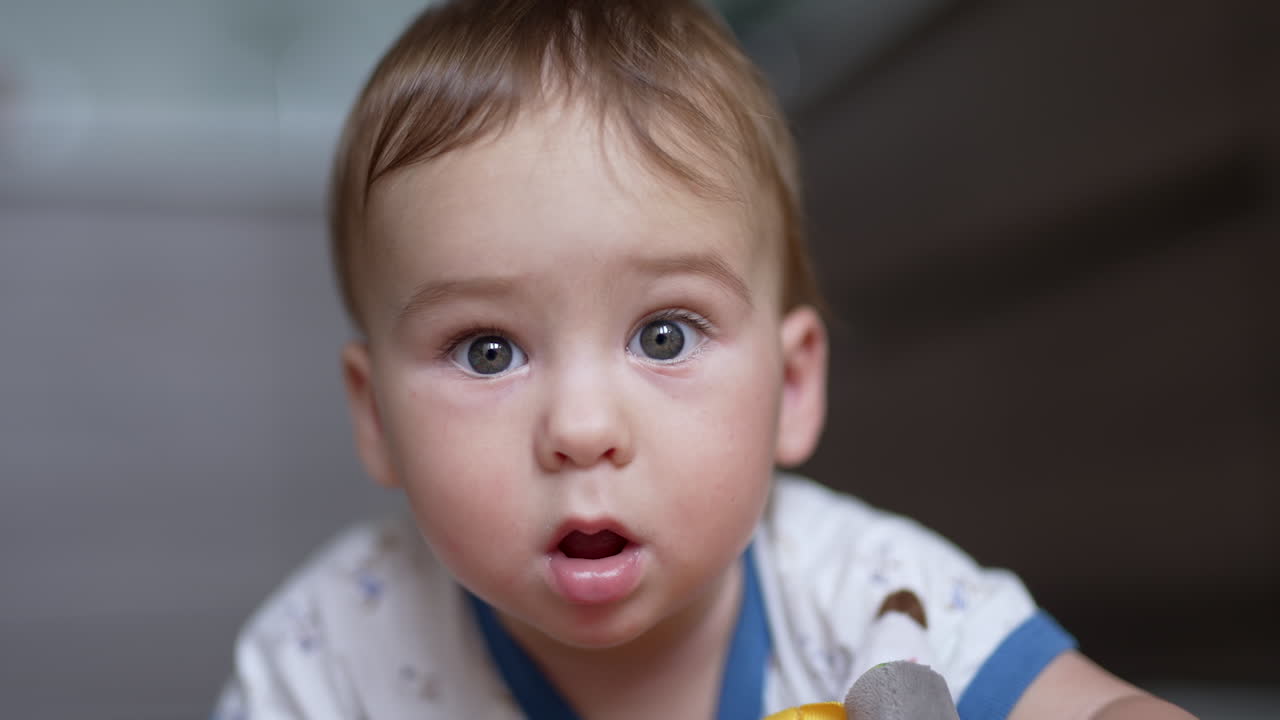 Little cute grey-eyed baby boy looking at camera. Portrait of a lovely Caucasian kid close up. Blurred backdrop.