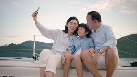 an asian family consisting of parents and children taking selfies on yachts with smartphones during vacation time.