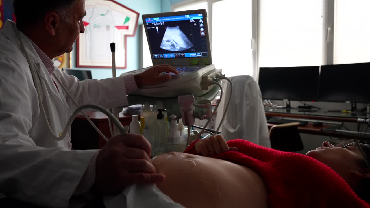 Gynecologist lowers the ultrasound screen so his pregnant patient could see the baby