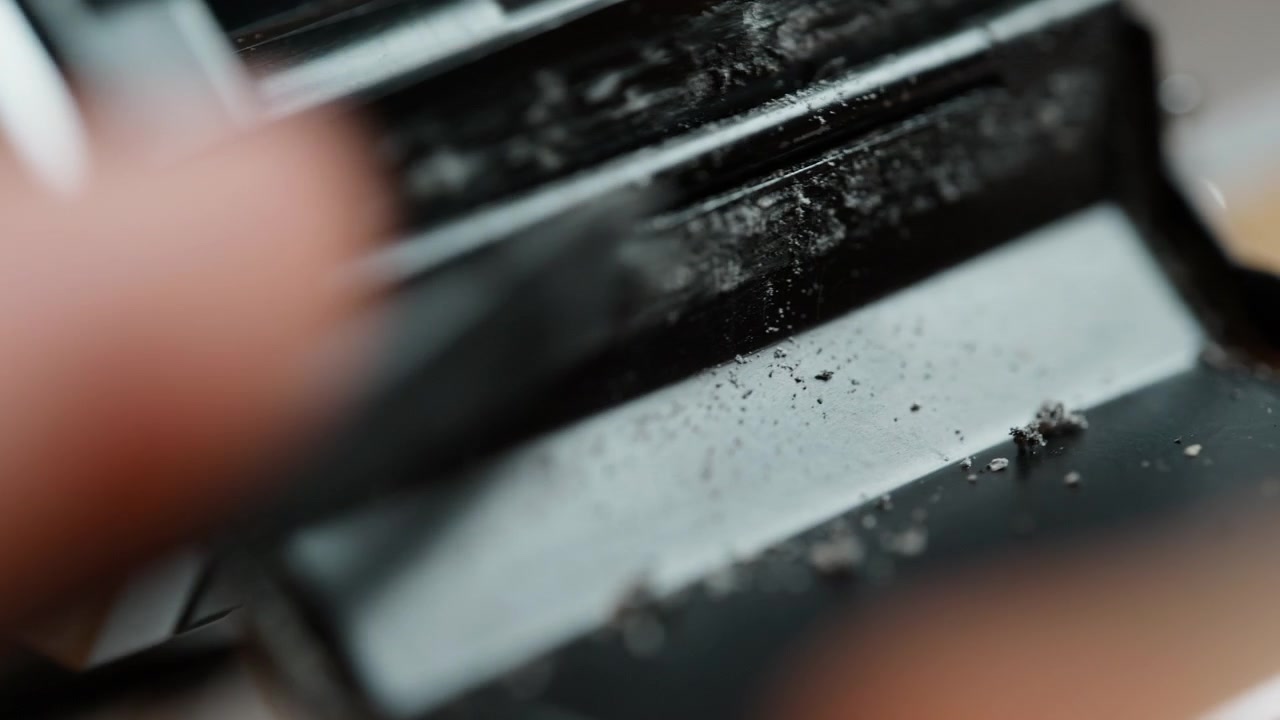 Macro shot with shallow depth of field: a tool scrapes crumbled old light seals from a vintage 35mm camera, the sharp focus falling off into soft bokeh. Detailed restoration of analog gear before rene