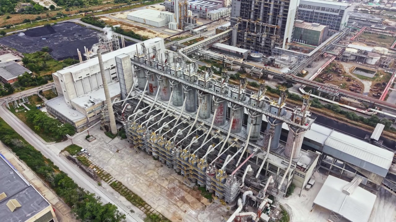 Impianto industriale situato in una vasta area manifatturiera con strutture alte e macchinari in funzione durante le ore diurne