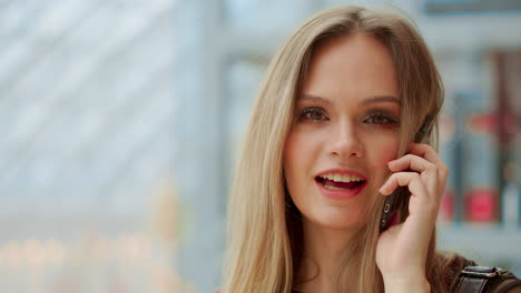 Hermosa-Chica-Hablando-Por-Un-Teléfono-Móvil-Mirando-A-La-Cámara-Y-Sonriendo.-Venta,-Consumismo:-Mujer-Joven-Con-Smartphones-Y-Bolsas-De-Compras-Parada-Y-Hablando-Cerca-Del-Centro-Comercial