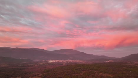 vuelo lateral de un avión no tripulado sobre un valle rodeado de montañas y en el que hay varias ciudades a la hora de la puesta del sol con nubes rosadas naranja y violeta en ávila, españa