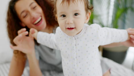 Happy,-mother-and-baby-playing-on-bed-holding