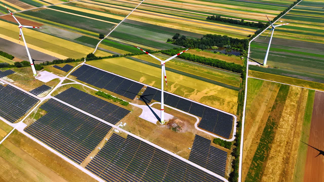 Wind and solar energy scene. Wind turbines tower over expansive solar panel fields in a vibrant, green agricultural landscape at midday