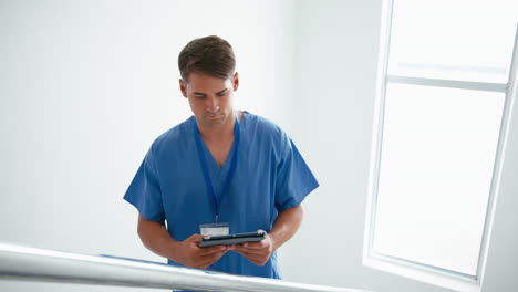 Male-Doctor-Or-Nurse-With-Digital-Tablet-Checking-Patient-Notes-On-Stairs-In-Hospital