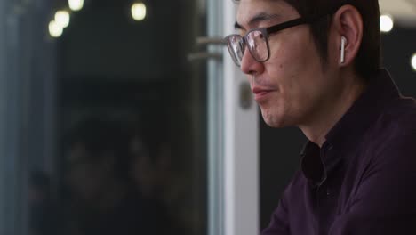 Asian-man-wearing-wireless-earphones-having-a-video-call-on-smartphone-while-sitting-at-a-cafe