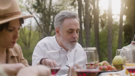 middle aged caucasian man eating and talking to his friends sitting at table during an outdoor party in the park