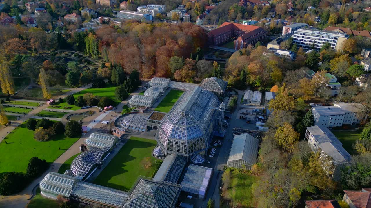 Berlin botanical garden Dome construction glasshouses surrounded by autumn trees and city landscape. Beautiful aerial view flight fly reverse drone shot from above