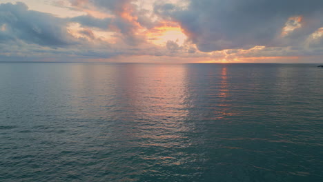 sun rays breaking grey clouds at evening. aerial tranquil ocean sunset horizon