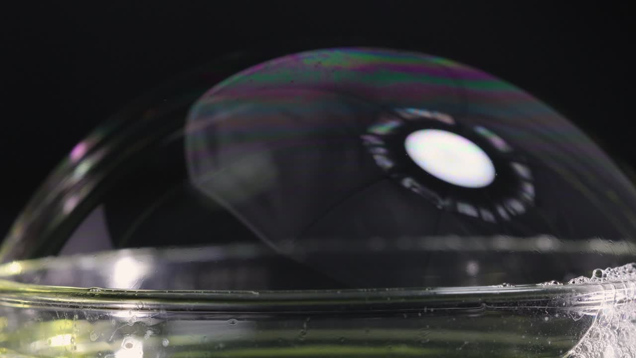 A soap bubble bursts, showcasing vibrant color reflections against a dark background, captured in slow motion
