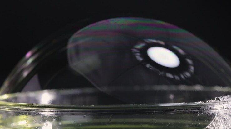A soap bubble bursts, showcasing vibrant color reflections against a dark background, captured in slow motion