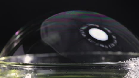 a soap bubble bursts, showcasing vibrant color reflections against a dark background, captured in slow motion