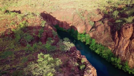 drone footage flying left to right revealing a deep red gorge with a calm river flowing through it