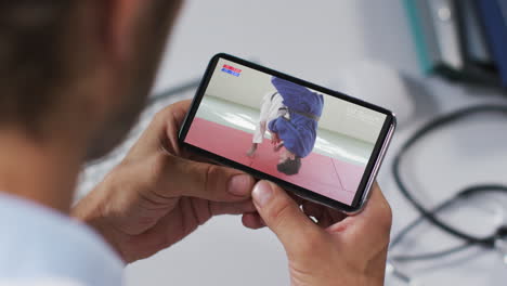 composición de un médico masculino viendo un partido de judo en un teléfono inteligente