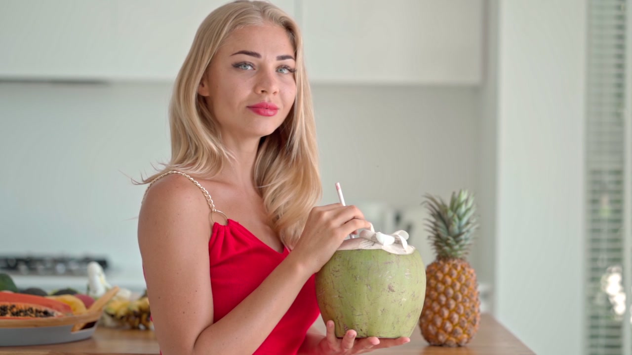Giovane donna che beve acqua di cocco fresca in una cucina moderna