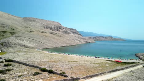 an aerial lift off over karst, white barren landscape and green cove with beach, island pag, croatia summer day