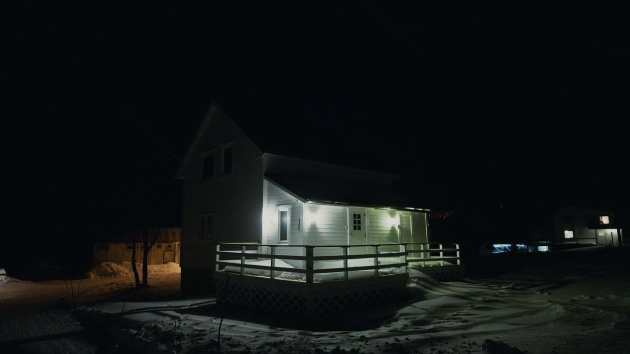Weißes arktisches Haus, nachts beleuchtet, mit schneebedecktem Garten und Terrasse