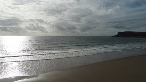 Luftaufnahme-Der-Sonnenreflexion-Auf-Dem-Meer,-Während-Die-Wellen-Sanft-Auf-Den-Mewslade-Strand-Auf-Der-Gower-Halbinsel-Rollen---4K-Drohnenaufnahme