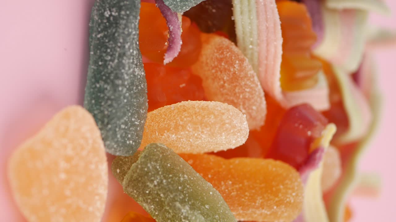 Nærbilde av assorterte fargerike sukkertøybelagte gummibiter som roterer på rosa bakgrunn