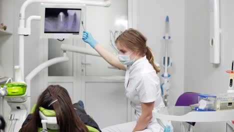 Healthy-teeth-and-dental-healthcare.-Confident-professional-doctor-dentist-is-showing-x-ray-teeth-on-a-tablet.-Female-dentist-in-mask-and-lab-coat.