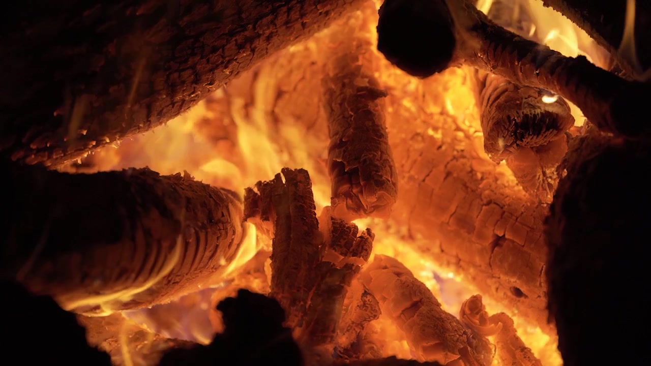 Primo piano ripreso a mano di fiamme arancioni incandescenti che tremolano tra ceppi di legno che bruciano all'interno di un accogliente falò di notte.