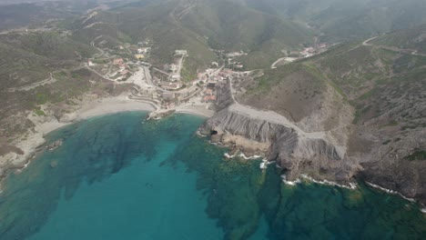 Aerial-high-altitude-backward-shot-over-the-blue-lagoon-and-the-abandoned-former-silver-mines-on-the-Argentiera-cape-in-Sardinia,-Italy