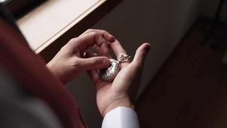 close up groom gently holding engraved vintage pocket watch near window