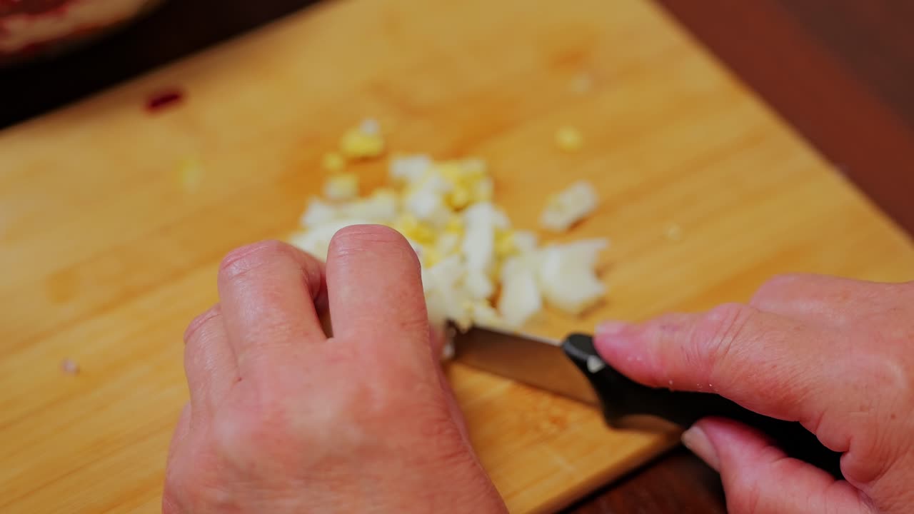 Close-up of knife slicing boiled eggs into pieces for rustic homemade salad