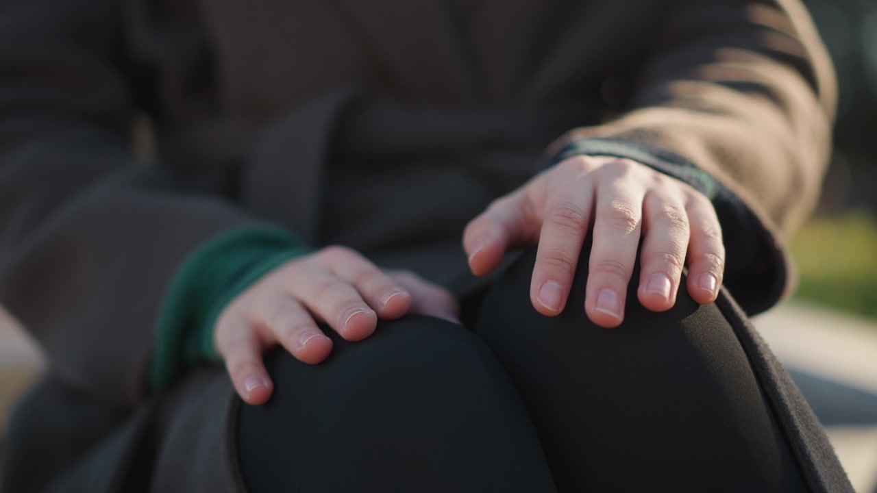 Primo piano di una persona che poggia le mani sulle ginocchia all'aperto.