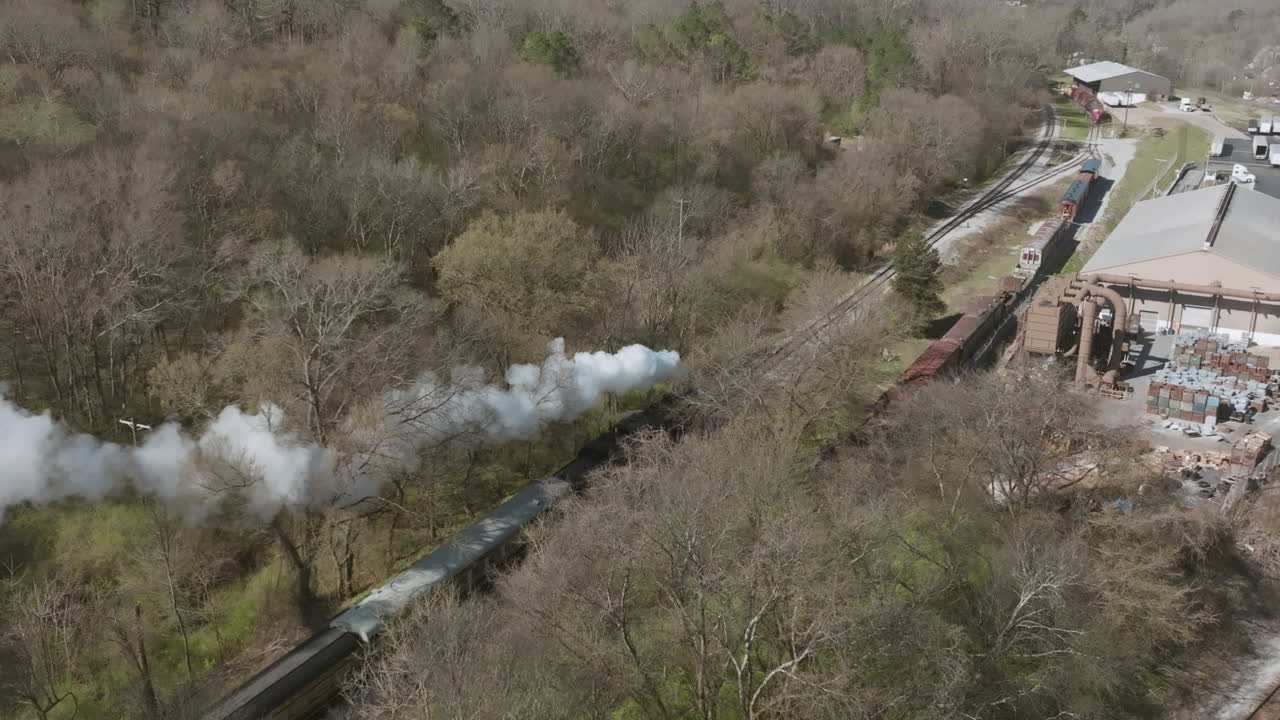toma aérea de un motor de tren de vapor pasando por una fábrica
