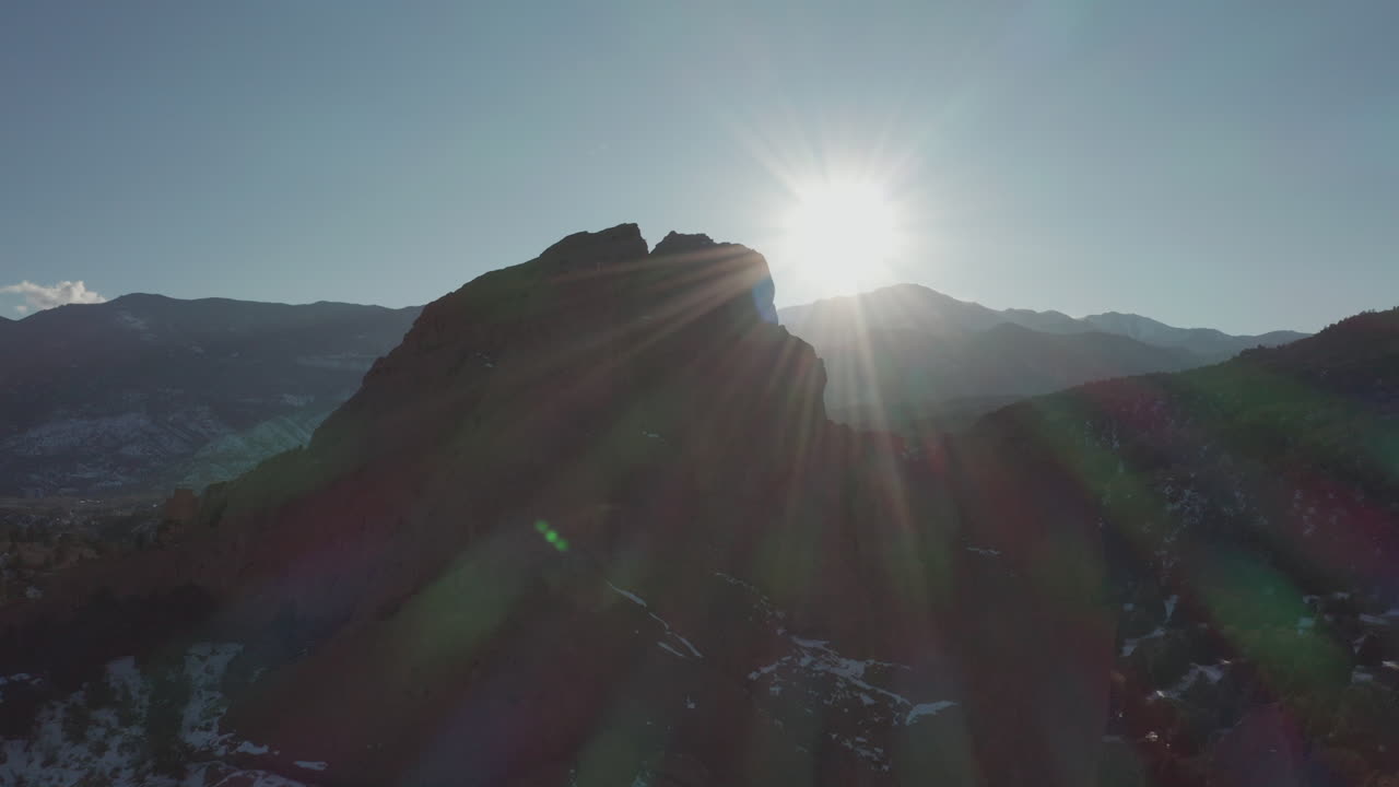 Aerial dolly forward toward red rock silhouette with sun spot