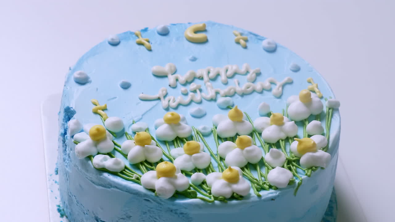 노란색  ⁇ 과 녹색 억양으로 작은  ⁇ 색 꽃으로 장식 된 파란색 얼음 생일 케이크의 클로즈업  ⁇ 에서 확대