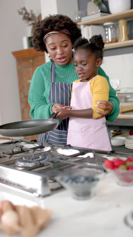 vertical video of african american mother and daughter frying pancakes in kitchen, slow motion