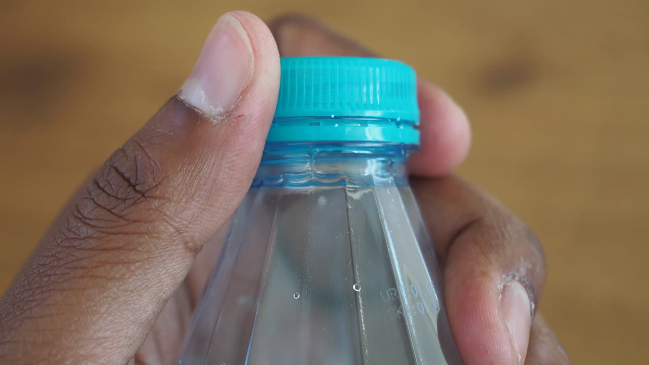 mano sosteniendo una botella de agua de plástico con tapa azul azul