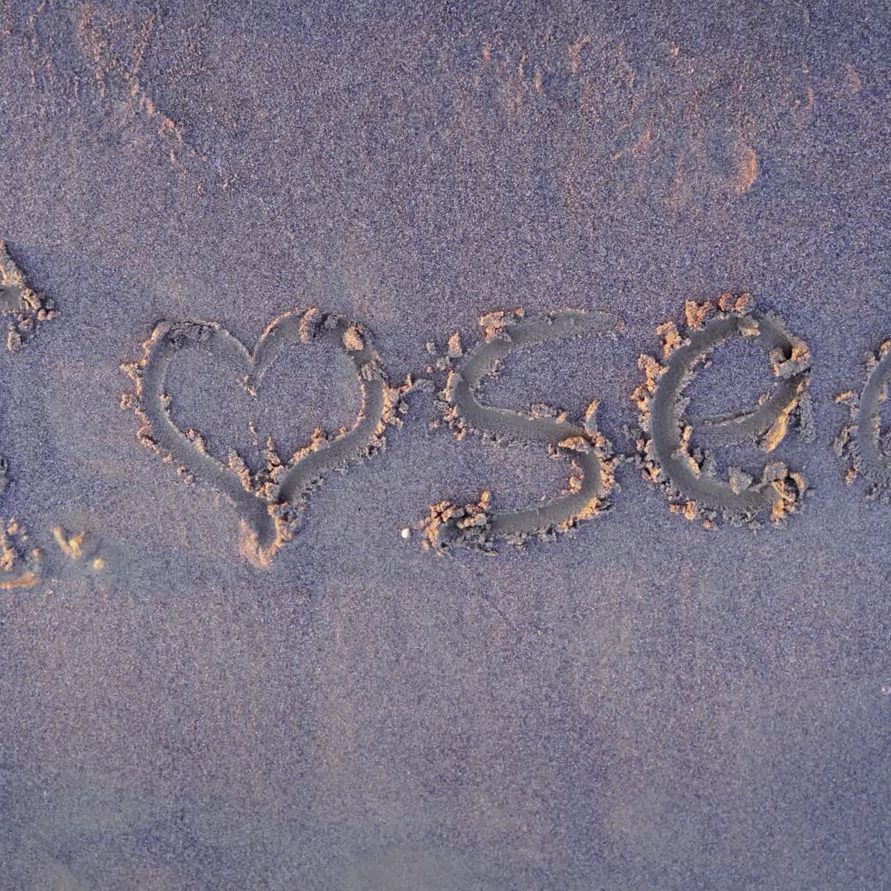 Handwritten drawings on sandy beach. Water waves breaking the symbol on sand and wash it away. Top view.