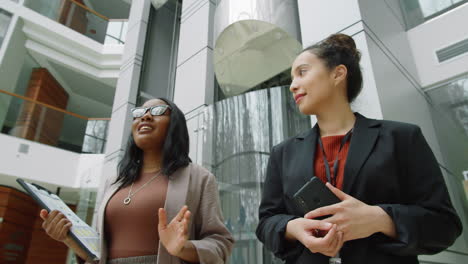 diverse female colleagues walking in office center and speaking