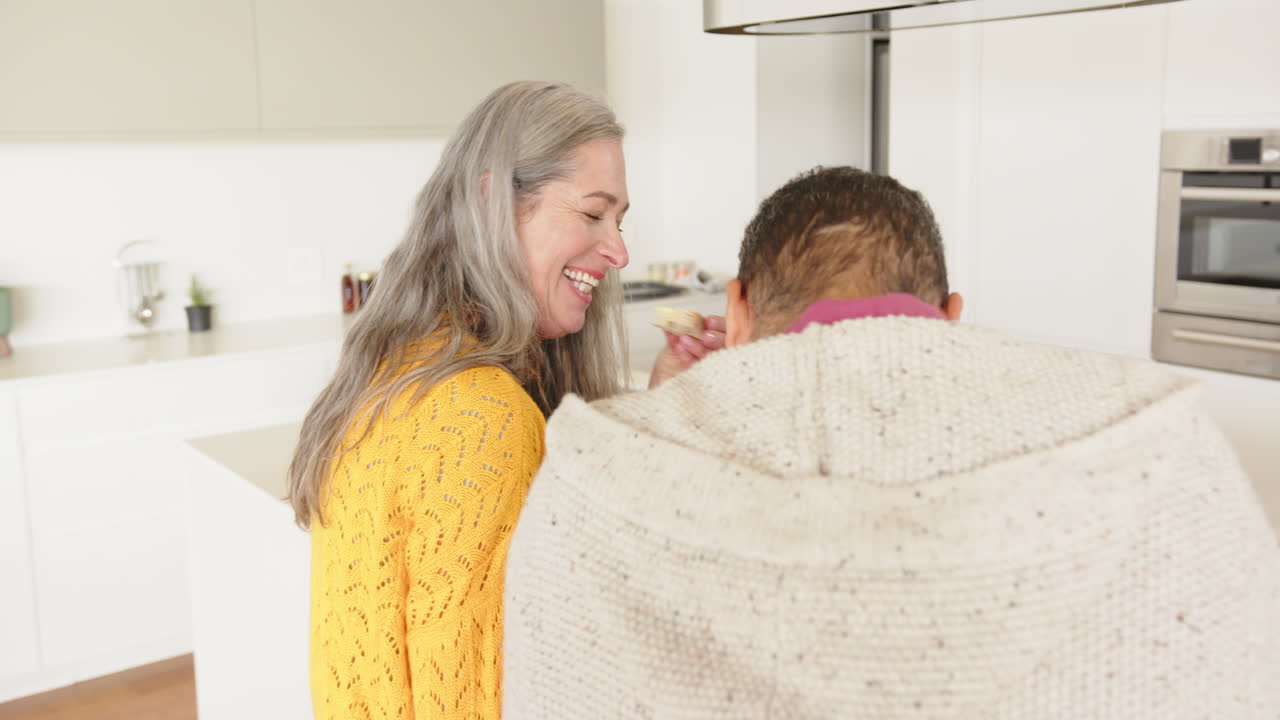 Smiling woman in yellow sweater interacting with partner in modern kitchen, at home